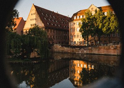 Blick durch ein rundes Element auf eine Häuserzeile am Wasser.