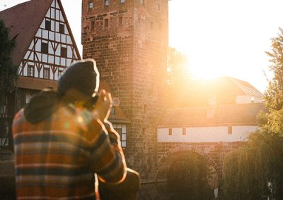 Fotograf steht am Wasser, im Hintergrund ein Turm bei Sonnenaufgang.