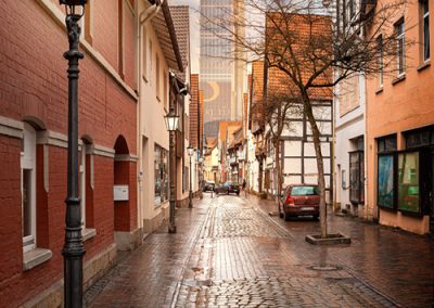 Kopfsteinpflastergasse in einer deutschen Altstadt mit Blick auf futuristischen Turm.