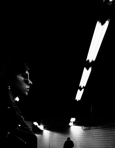 Frau mit Sonnenbrille in dunklem U-Bahn-Tunnel, Person im Hintergrund.