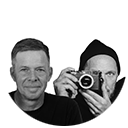 Schwarz-weiß Porträt von zwei Männern: Jan Dittmer mit kurzem Haar lächelt in die Kamera, Chris Frenz im Beanie hält eine Kamera vors Gesicht