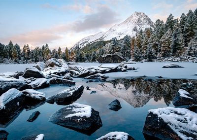 Verschneite Berglandschaft mit spiegelndem See und ruhigem Winterlicht.
