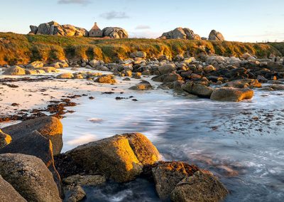 Felsige Küstenlandschaft im warmen Abendlicht mit ruhigem Wasser und langen Belichtungszeiten.