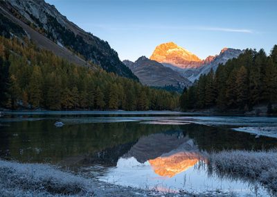 Berglandschaft mit spiegelndem See und beleuchtetem Gipfel im Morgenlicht.