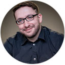 Dennis Weismantel mit Kamera, lächelnd im Freien – authentisches Portrait eines Fotografen