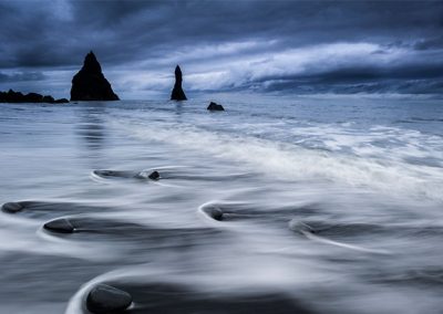Dramatische Küstenlandschaft mit dunklem Himmel, Felsen im Meer und weichen Wasserbewegungen durch Langzeitbelichtung.
