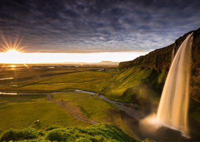 Großer Wasserfall im warmen Abendlicht mit weiter Landschaft und tief stehender Sonne.