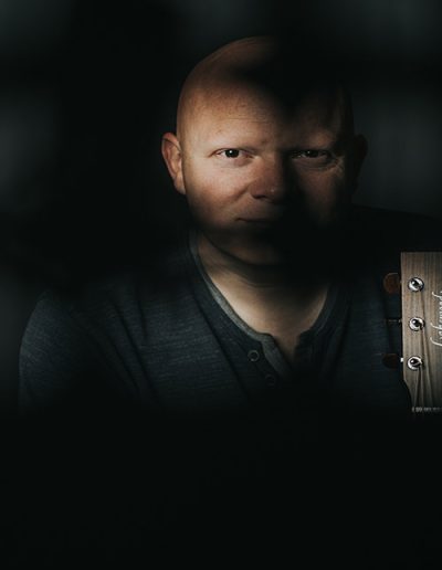 Mann im Halbschatten mit Gitarre, dunkle Stimmung.