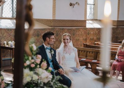 Hochzeitspaar in Kirchenbank während der Trauung, mit Kerzenlicht – fotografiert von Dennis Weissmantel.