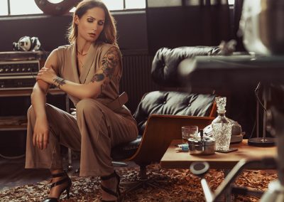 Frau mit Tattoos sitzt in stilvoller Retro-Lounge mit Vintage-Möbeln und Studiolicht