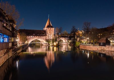 Nachtaufnahme mit Brücke, Turm und Spiegelung im Wasser in der Altstadt Nürnbergs.
