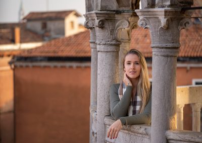 Frau lehnt an einer steinernen Balustrade in historischer Stadtumgebung, fotografiert bei goldenem Licht.