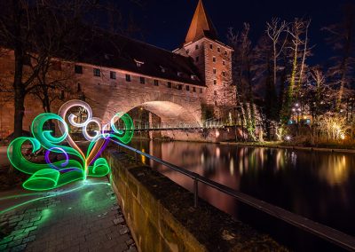 Farbiges Lightpainting mit grünen Lichtformen vor mittelalterlicher Steinbrücke.