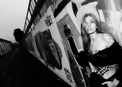 Frau lehnt an Graffiti-Wand in schräger Perspektive, Schwarzweißaufnahme.