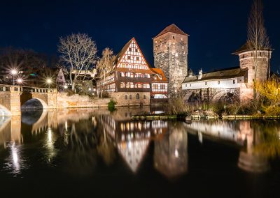Henkersteg und Weinstadel spiegeln sich bei Nacht in der Pegnitz.
