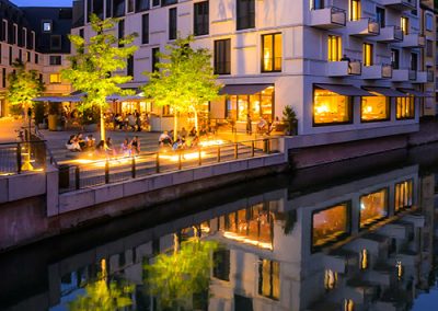 Moderne Architektur am Fluss, warm beleuchtet bei Abenddämmerung.