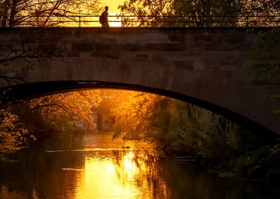 Silhouette einer Person auf Brücke bei Sonnenuntergang, Spiegelung im Wasser.