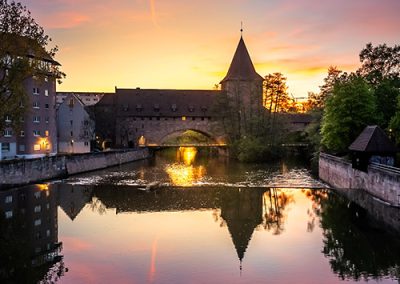 Blick auf Fluss und Stadtmauer bei Sonnenuntergang, Spiegelung im Wasser.
