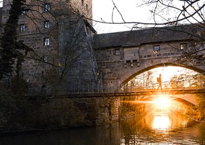 Alte Steinbrücke mit Turm im Hintergrund, Sonne scheint durch das Brückenbogen.