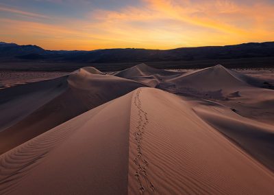 Dünenlandschaft bei Sonnenuntergang mit Fußspuren im Sand, fotografiert von Nicolas Alexander Otto.