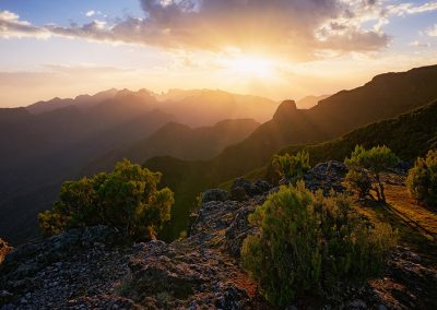 Sonnenuntergang hinter einer Gebirgskette, dramatisch beleuchtete Wolken und Landschaft.