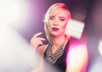 Blonde Frau mit auffälliger Halskette, aufgenommen in kreativem Studio-Licht mit Bokeh-Effekten