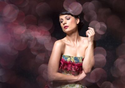 Model in floralem Kleid, inszeniert mit dramatischem Bokeh-Hintergrund in warmen Tönen