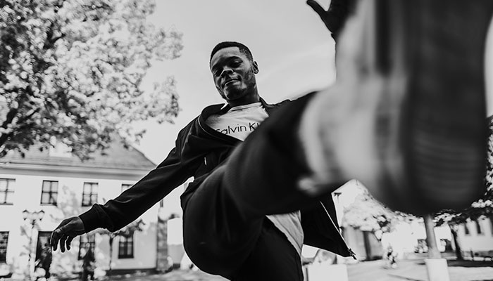 Schwarz-Weiß-Aufnahme eines Mannes in urbaner Umgebung, der dynamisch mit erhobenem Bein in die Kamera posiert – Beispiel für urbane Portraitfotografie.