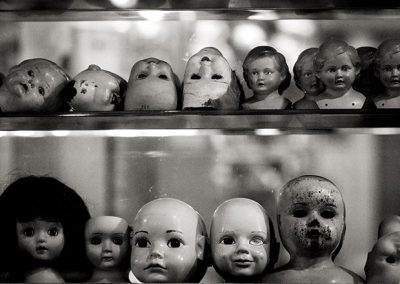 Schwarz-Weiß-Aufnahme einer Vitrine mit alten Puppenköpfen und Puppenfiguren.