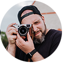 Dennis Weismantel mit Kamera, lächelnd im Freien – authentisches Portrait eines Fotografen