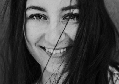 Frau lächelt in die Kamera, Schwarz-Weiß-Nahaufnahme mit Haaren im Gesicht.