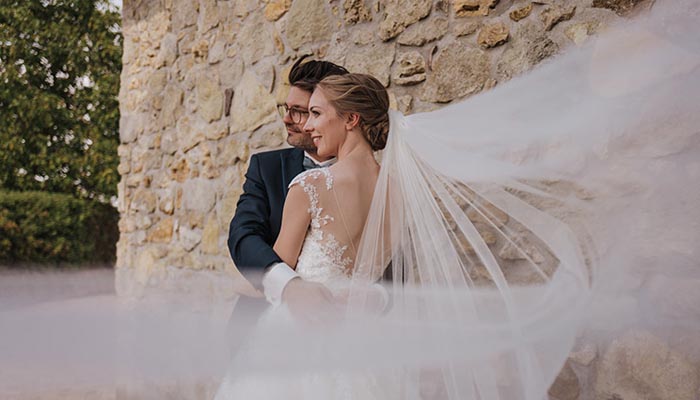 Du siehst ein Brautpaar beim Paarshooting vor einer Steinmauer – Momentaufnahme aus einem Hochzeitsfotografie-Workshop