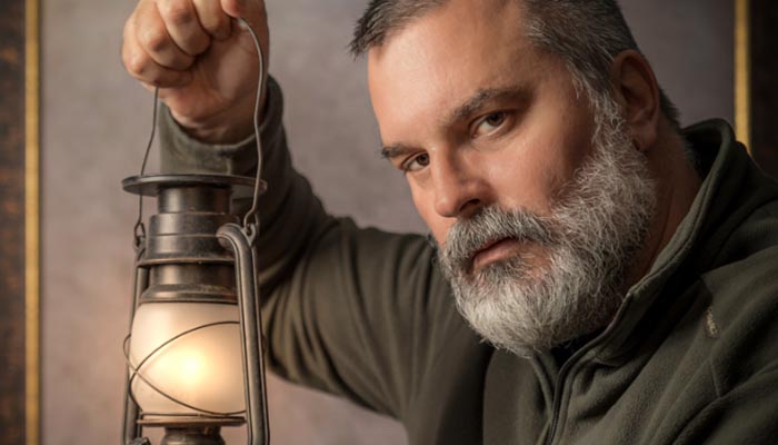Porträt eines Mannes mit grauem Bart, der eine Lampe hält – inszenierte Lichtstimmung als Beispiel für intensive Bildwirkung