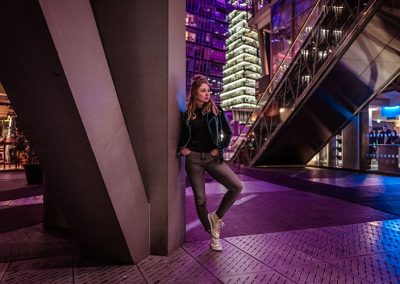 Frau lehnt an moderner Architektur bei Nacht, Neonlichter spiegeln die Großstadtstimmung.